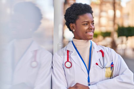 Téléchargez les photos : Femme afro-américaine portant l'uniforme de médecin debout avec les bras croisés geste à la rue - en image libre de droit