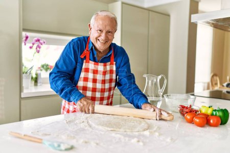Téléchargez les photos : Senior homme souriant confiant clavier pâte à pizza à la cuisine - en image libre de droit