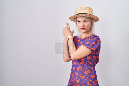 Foto de Mujer caucásica joven con vestido de flores y sombrero de verano sosteniendo arma simbólica con gesto de mano, jugando a matar armas de fuego, cara enojada - Imagen libre de derechos