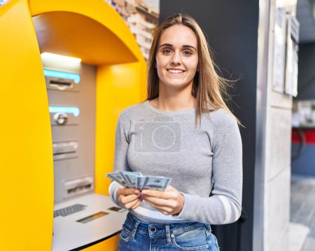 Photo for Young blonde woman smiling confident holding dollars on cashier at street - Royalty Free Image