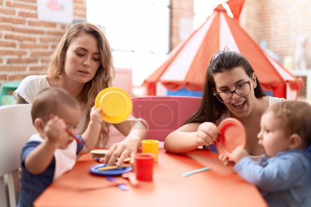 Foto de Profesores y estudiantes de preescolar aprendiendo a comer sentados en la mesa en el jardín de infantes - Imagen libre de derechos