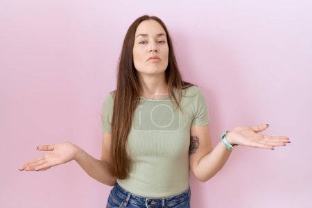 Photo for Beautiful brunette woman standing over pink background clueless and confused with open arms, no idea concept. - Royalty Free Image