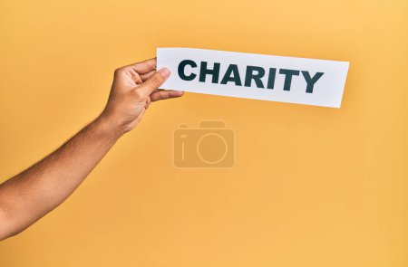 Photo for Hand of caucasian man holding paper with charity word over isolated yellow background - Royalty Free Image