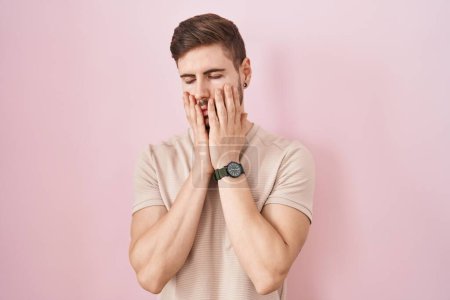 Foto de Hombre hispano con barba de pie sobre fondo rosa manos cansadas cubriendo la cara, depresión y tristeza, molesto e irritado por el problema - Imagen libre de derechos
