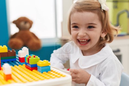 Photo for Adorable caucasian girl playing with construction blocks sitting on table at kindergarten - Royalty Free Image