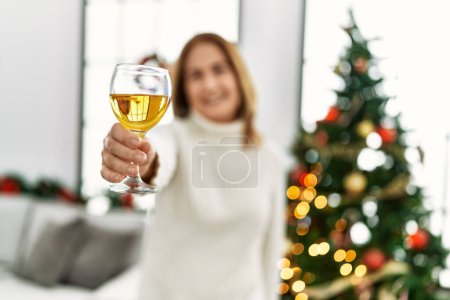Foto de Mujer caucásica de mediana edad brindando con champán de pie junto al árbol de Navidad en casa - Imagen libre de derechos