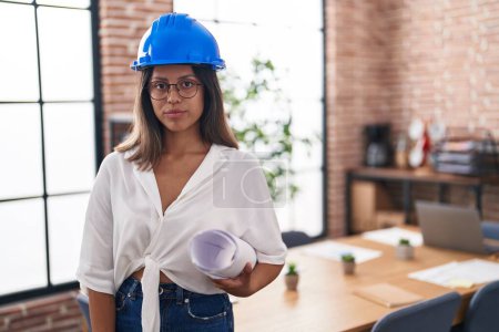 Photo for Hispanic young woman wearing architect hardhat at office thinking attitude and sober expression looking self confident - Royalty Free Image