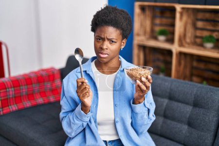 Foto de Mujer afroamericana comiendo cereales integrales saludables expresión despistada y confusa. concepto de duda. - Imagen libre de derechos
