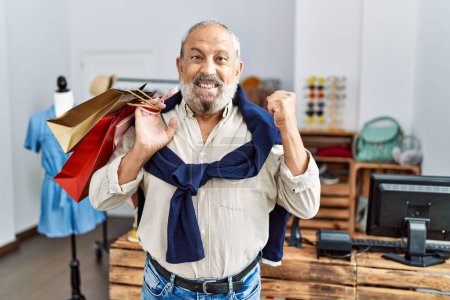 Photo for Handsome senior man holding shopping bags at boutique shop screaming proud, celebrating victory and success very excited with raised arms - Royalty Free Image