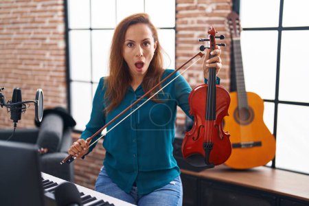 Photo for Brunette woman playing violin afraid and shocked with surprise and amazed expression, fear and excited face. - Royalty Free Image