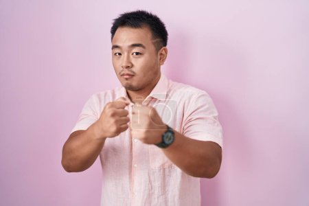 Téléchargez les photos : Chinese young man standing over pink background ready to fight with fist defense gesture, angry and upset face, afraid of problem - en image libre de droit