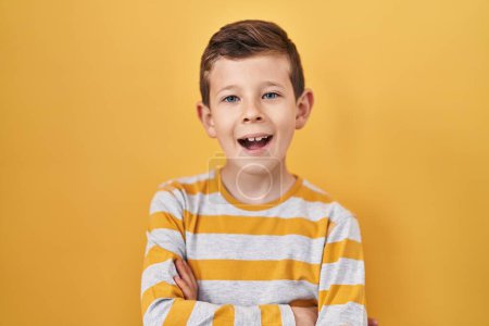 Téléchargez les photos : Young caucasian kid standing over yellow background happy face smiling with crossed arms looking at the camera. positive person. - en image libre de droit