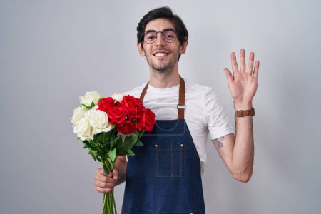 Photo for Young hispanic man holding bouquet of white and red roses waiving saying hello happy and smiling, friendly welcome gesture - Royalty Free Image