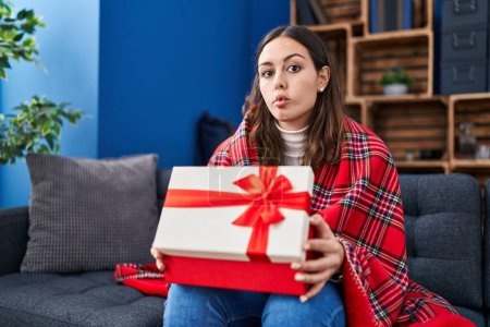Photo for Young hispanic woman opening gift box making fish face with mouth and squinting eyes, crazy and comical. - Royalty Free Image