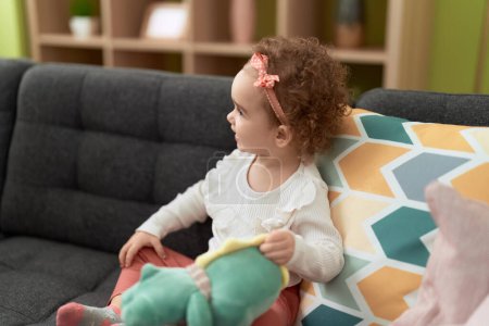 Téléchargez les photos : Adorable fille caucasienne jouer avec poupée assis sur le canapé à la maison - en image libre de droit