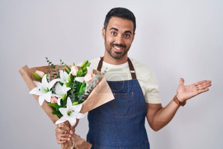 Téléchargez les photos : Homme hispanique avec barbe travaillant comme fleuriste pointant de côté avec les mains ouvertes paumes montrant l'espace de copie, présentant la publicité souriant heureux heureux - en image libre de droit