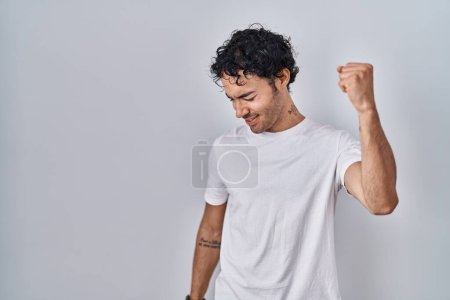 Foto de Hombre hispano parado sobre fondo aislado bailando feliz y alegre, sonriendo moviéndose casual y confiado escuchando música - Imagen libre de derechos