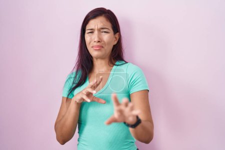 Foto de Mujer hispana joven de pie sobre fondo rosa expresión disgustada, disgustada y temerosa haciendo cara de asco porque la reacción de aversión. - Imagen libre de derechos
