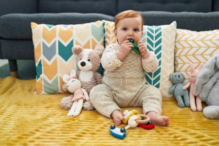 Foto de Adorable pelirroja niño mordiendo coche juguete sentado en el sofá en casa - Imagen libre de derechos