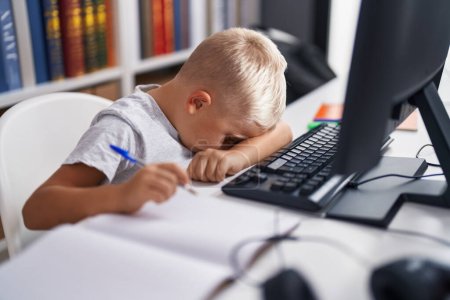 Téléchargez les photos : Adorable élève en bas âge stressé à l'aide d'un ordinateur assis sur la table en classe - en image libre de droit