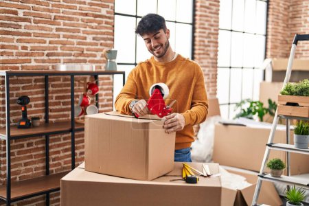 Photo for Young hispanic man smiling confident packing cardboard box at new home - Royalty Free Image