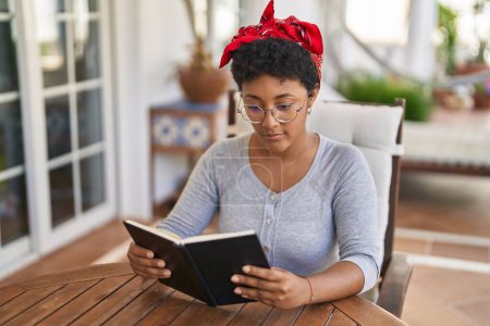Foto de Mujer afroamericana leyendo libro sentado en la mesa en casa terraza - Imagen libre de derechos