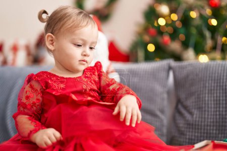 Foto de Adorable chica hispana sentada en el sofá junto al árbol de Navidad en casa - Imagen libre de derechos