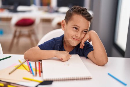 Photo for Adorable hispanic toddler student smiling confident sitting on table at classroom - Royalty Free Image