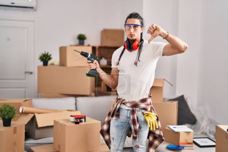 Photo for Hispanic man with long hair holding screwdriver at new home with angry face, negative sign showing dislike with thumbs down, rejection concept - Royalty Free Image
