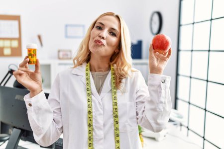 Photo for Beautiful blonde nutritionist woman holding fat pills looking at the camera blowing a kiss being lovely and sexy. love expression. - Royalty Free Image