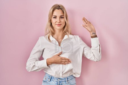 Téléchargez les photos : Young caucasian woman wearing casual white shirt over pink background swearing with hand on chest and open palm, making a loyalty promise oath - en image libre de droit