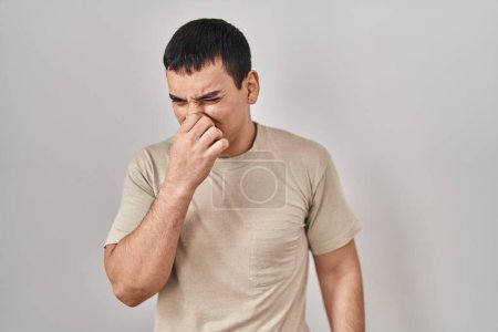 Téléchargez les photos : Jeune homme arabe portant un t-shirt décontracté sentant quelque chose de puant et dégoûtant, odeur intolérable, retenant son souffle avec les doigts sur le nez. mauvaise odeur - en image libre de droit