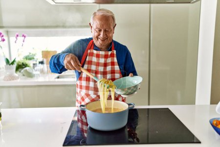 Foto de Hombre mayor sonriendo confiado cocinando espaguetis en la cocina - Imagen libre de derechos