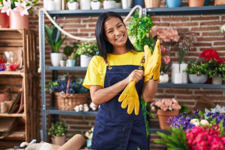 Photo for Young beautiful latin woman florist smiling confident wearing gloves at florist - Royalty Free Image