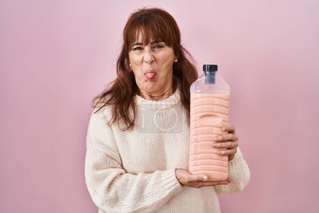 Photo for Middle age hispanic woman holding detergent bottle sticking tongue out happy with funny expression. - Royalty Free Image