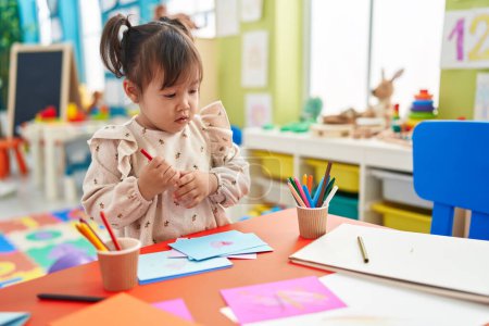 Photo for Adorable chinese girl preschool student drawing on paper standing at kindergarten - Royalty Free Image
