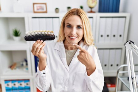 Téléchargez les photos : Belle femme dentiste blonde comparant le blanchiment des dents à la clinique souriant heureux pointant avec la main et le doigt - en image libre de droit