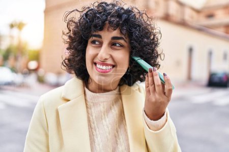 Foto de Young middle east woman excutive smiling confident listening audio message by smartphone at street - Imagen libre de derechos
