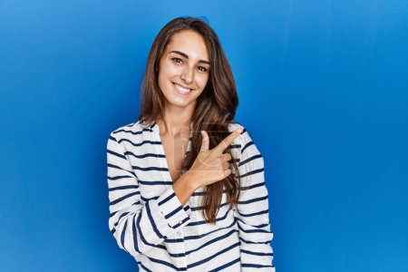 Téléchargez les photos : Jeune femme hispanique debout sur fond bleu isolé gai avec un sourire sur le visage pointant avec la main et le doigt vers le côté avec une expression heureuse et naturelle - en image libre de droit