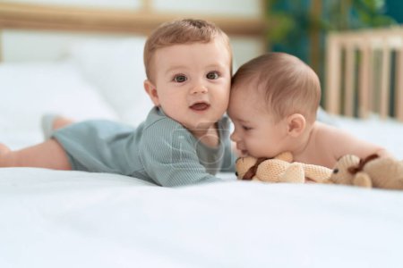 Photo for Two toddlers lying on bed playing with teddy bear at bedroom - Royalty Free Image