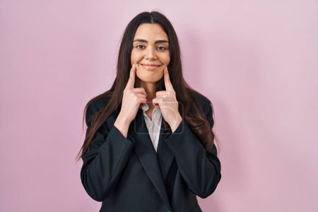 Foto de Young brunette woman wearing business style over pink background smiling with open mouth, fingers pointing and forcing cheerful smile - Imagen libre de derechos