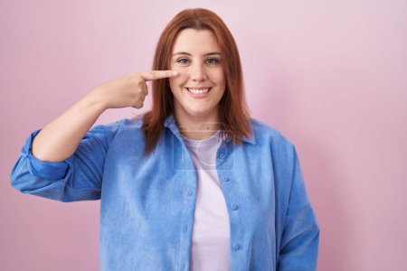 Photo for Young hispanic woman with red hair standing over pink background pointing with hand finger to face and nose, smiling cheerful. beauty concept - Royalty Free Image