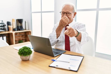 Photo for Senior man working at the office using computer laptop laughing at you, pointing finger to the camera with hand over mouth, shame expression - Royalty Free Image