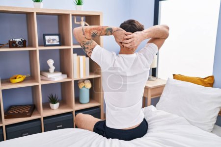 Foto de Young man waking up stretching arms on back view at bedroom - Imagen libre de derechos