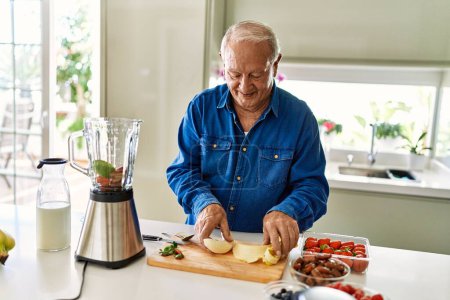 Téléchargez les photos : Senior homme souriant confiant tenant la banane pelée à la cuisine - en image libre de droit