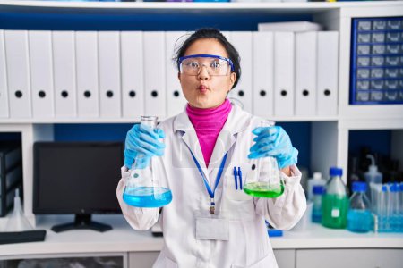 Foto de Young asian woman working at scientist laboratory making fish face with mouth and squinting eyes, crazy and comical. - Imagen libre de derechos