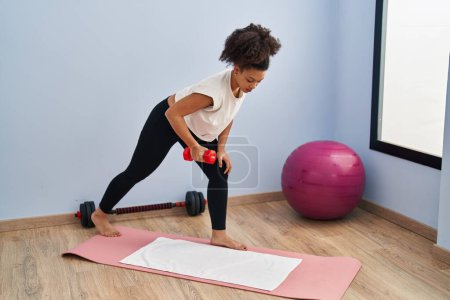 Photo for Young african american woman training using dumbbell at sport center - Royalty Free Image