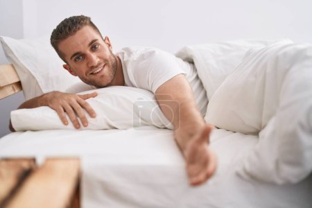Foto de Joven caucásico hombre haciendo venir gesto con la mano acostado en la cama en el dormitorio - Imagen libre de derechos