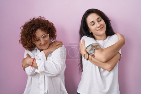 Téléchargez les photos : Mère et fille hispaniques portant un t-shirt blanc décontracté sur fond rose s'embrassant heureux et positif, souriant confiant. amour de soi et soins de soi - en image libre de droit
