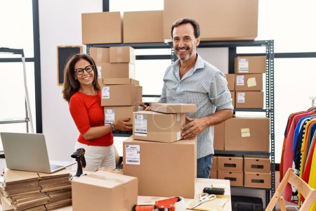 Middle age man and woman business partners smiling confident holding packages at storehouse